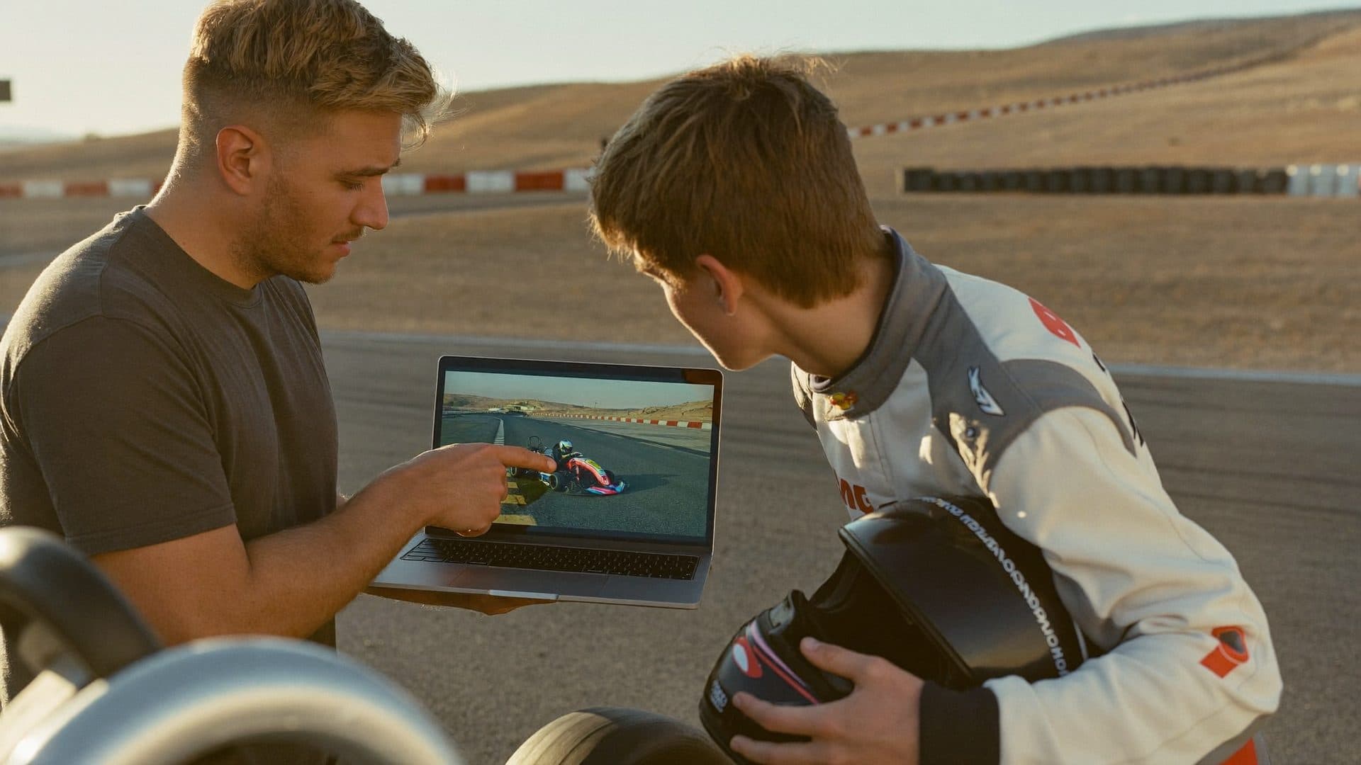 A coach and a young driver reviewing race footage on a laptop at the track